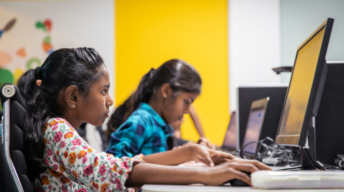 Side profile photo of two girls coding on computers