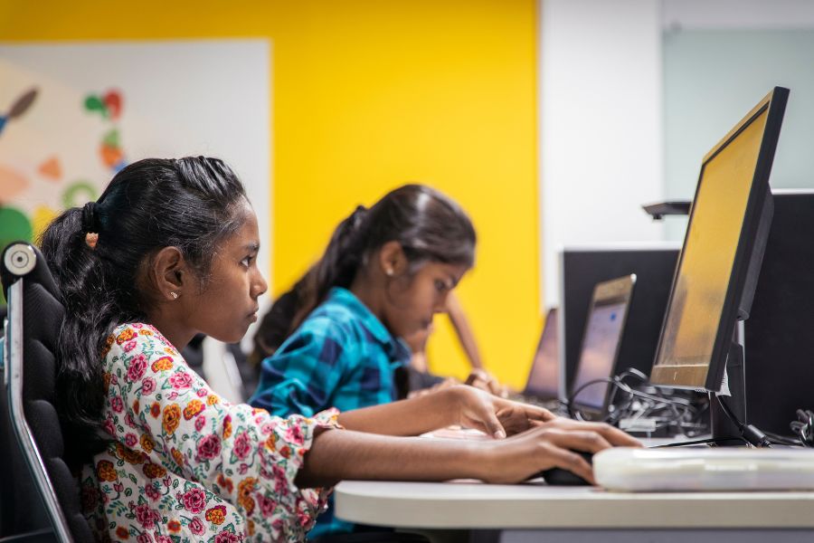 Side profile photo of two girls coding on computers