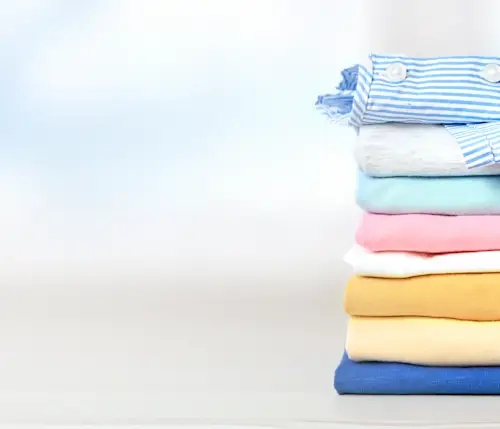 Zusammengelegte bunte Kleidung auf einem Tisch mit himmelblauem Hintergrund