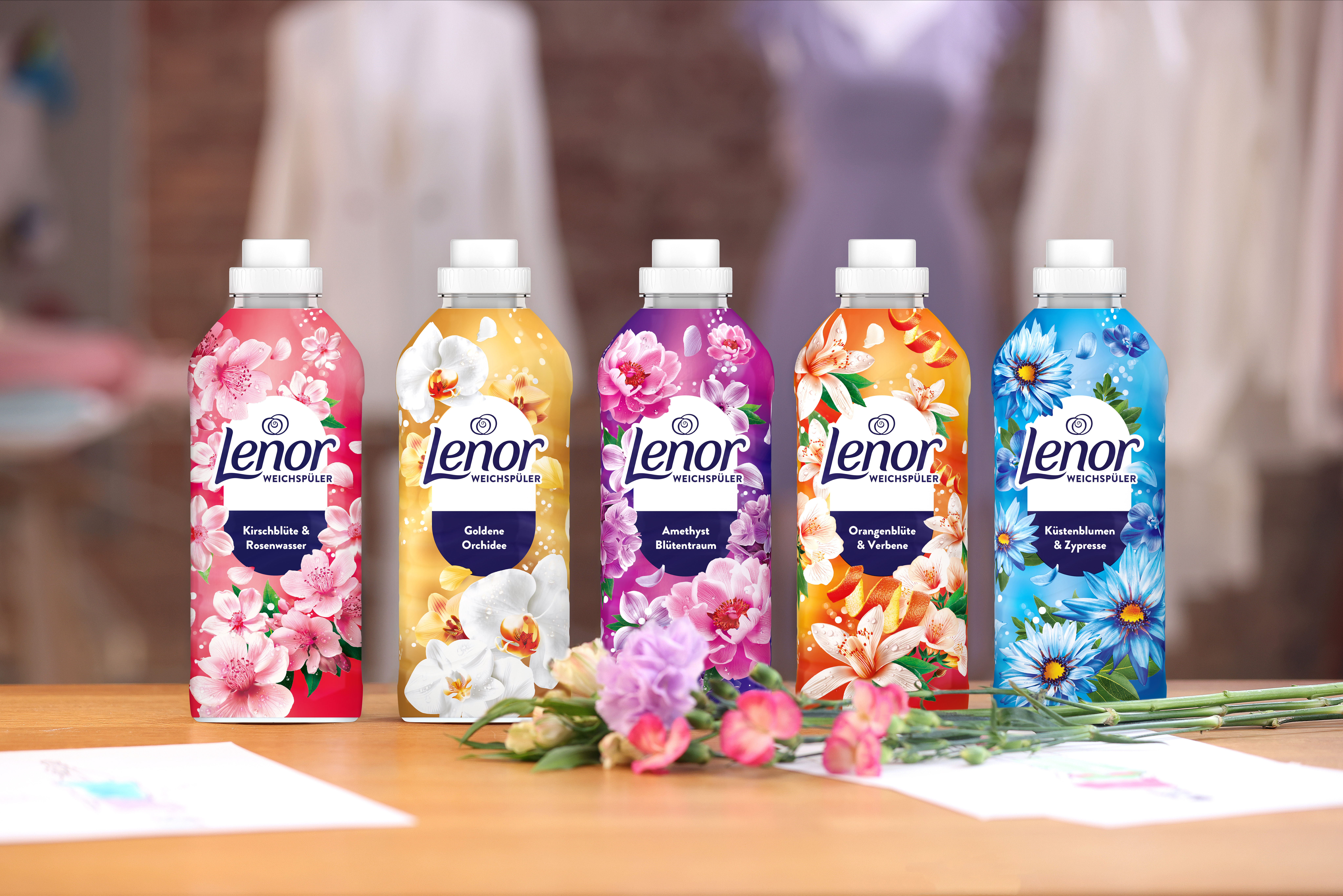 Fünf Lenor Weichspülerflaschen in verschiedenen Farben mit floralen Designs, jeweils für 32 Waschgänge.