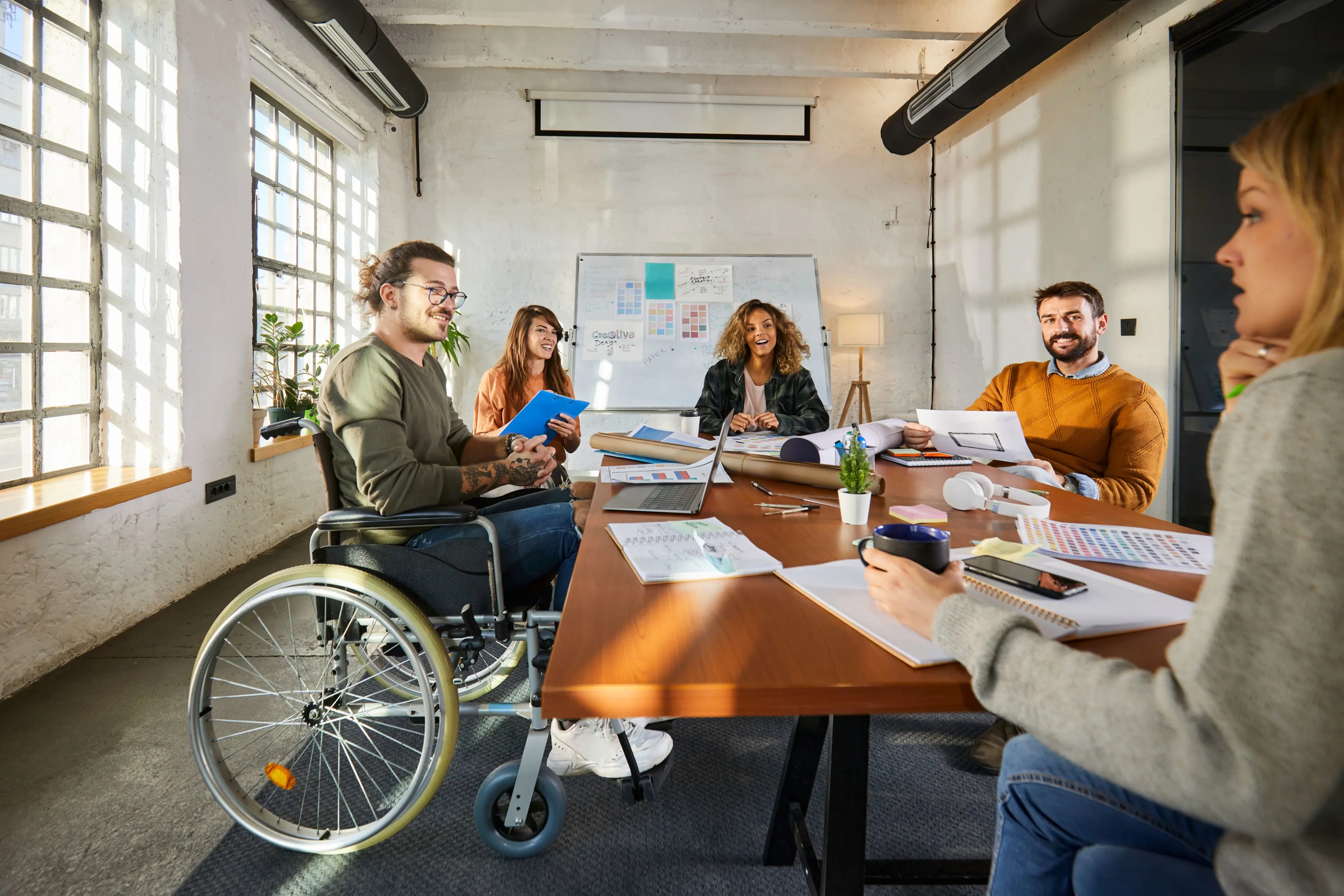 Cinq employés se réunissent dans une salle de conférence, dont un homme est en fauteuil roulant.