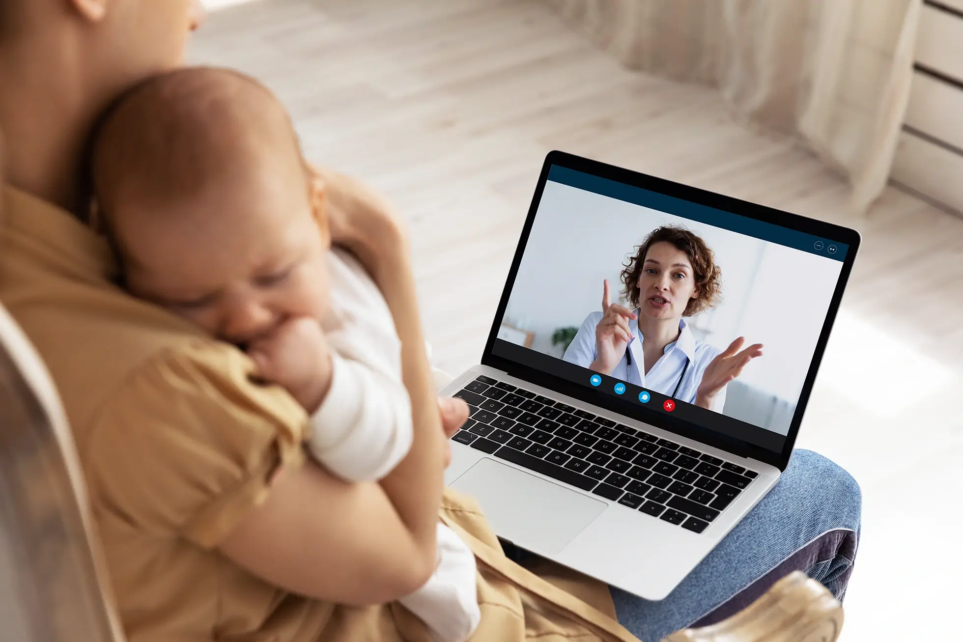 A woman is holding a baby while on a video call with a doctor.