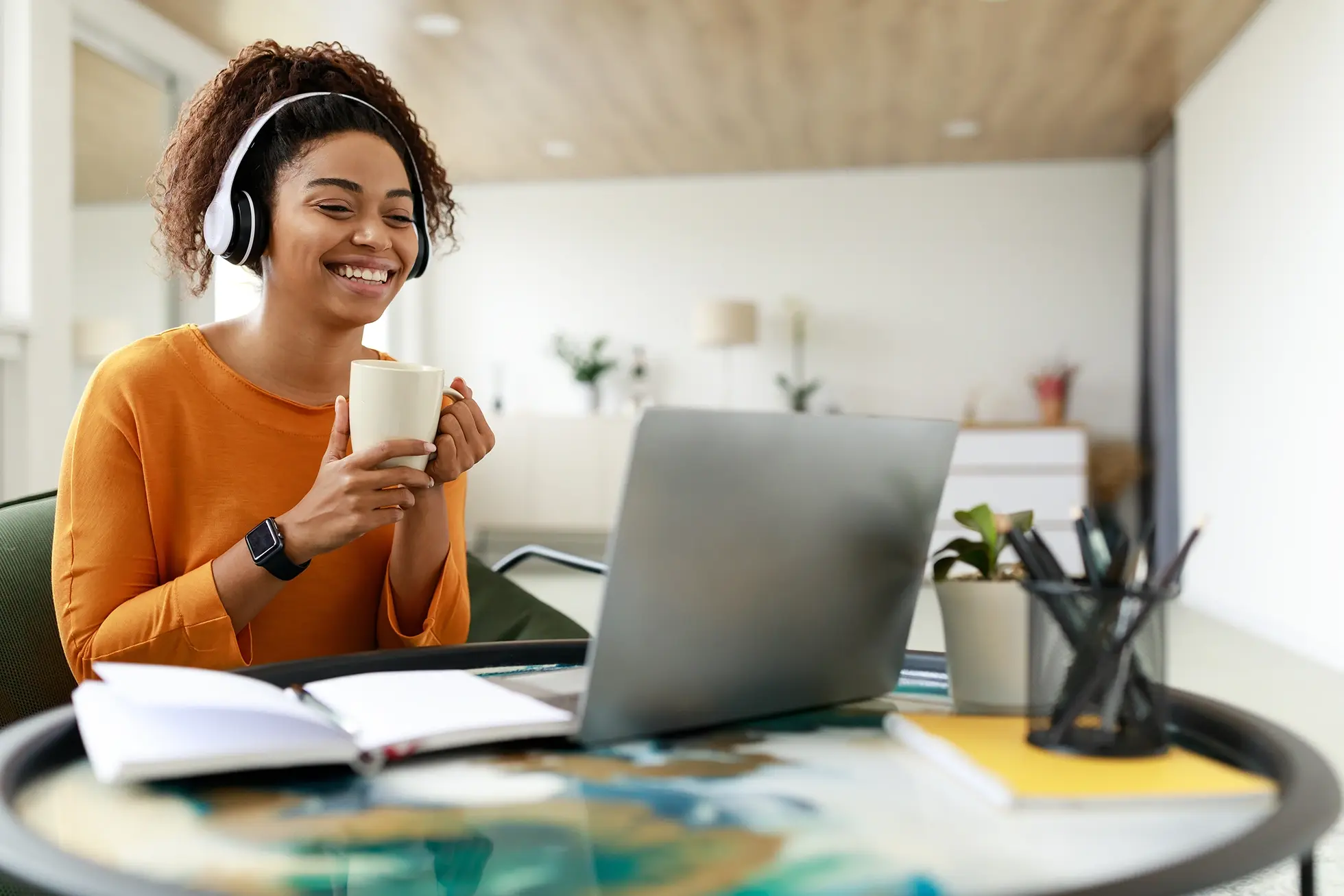 Young african american woman working at home with headphones and a cup of coffee.
