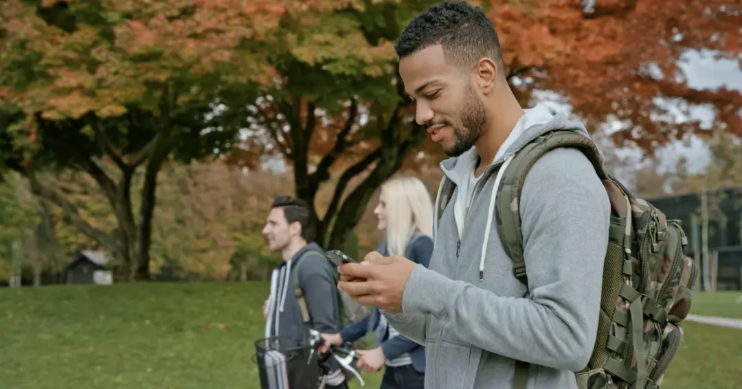 A young man walking on a school campus looking at his phone.