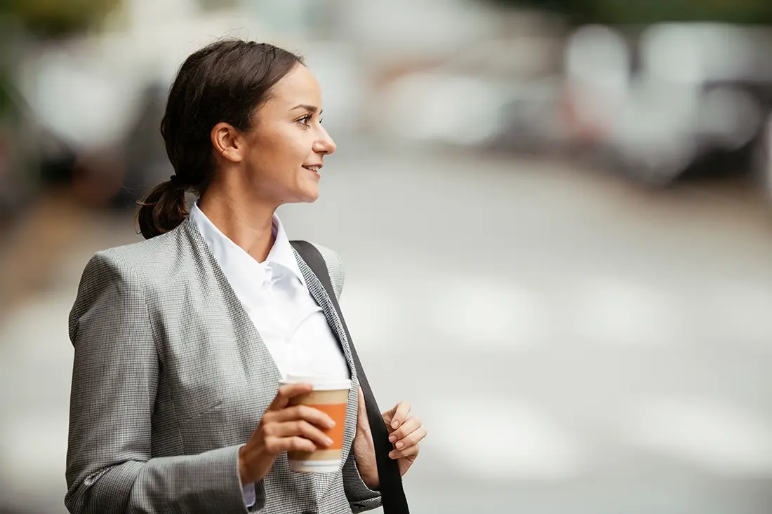 A business woman walking down the street with a cup of coffee.