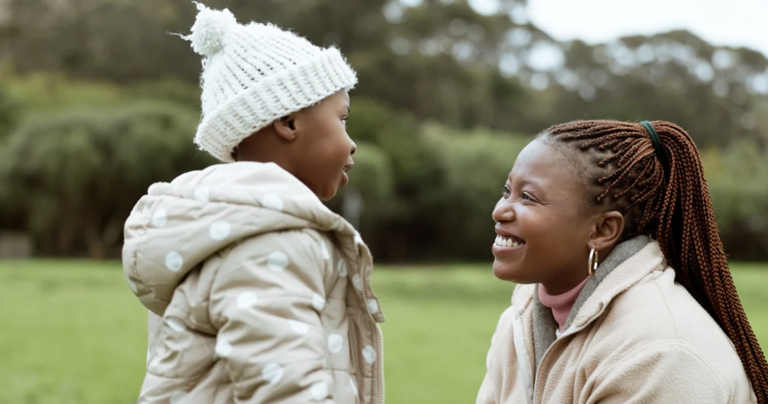 An african-american woman smiling, talking to her daughter in a park.