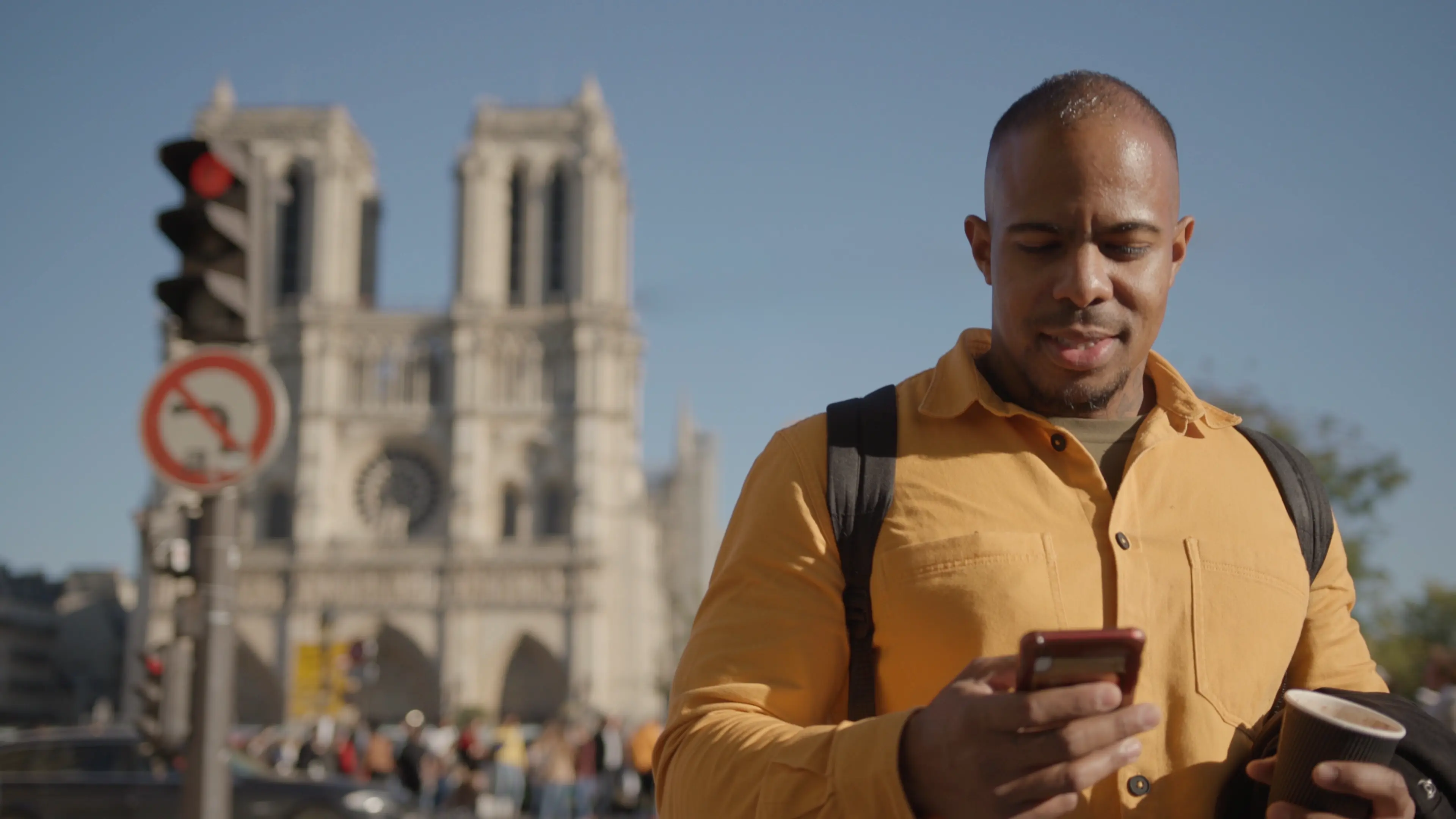 Un homme qui marche devant Notre Dame en regardant son téléphone.