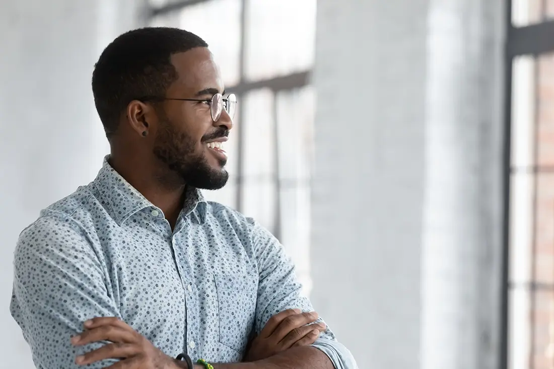 A young african american man with his arms crossed in front of a window.