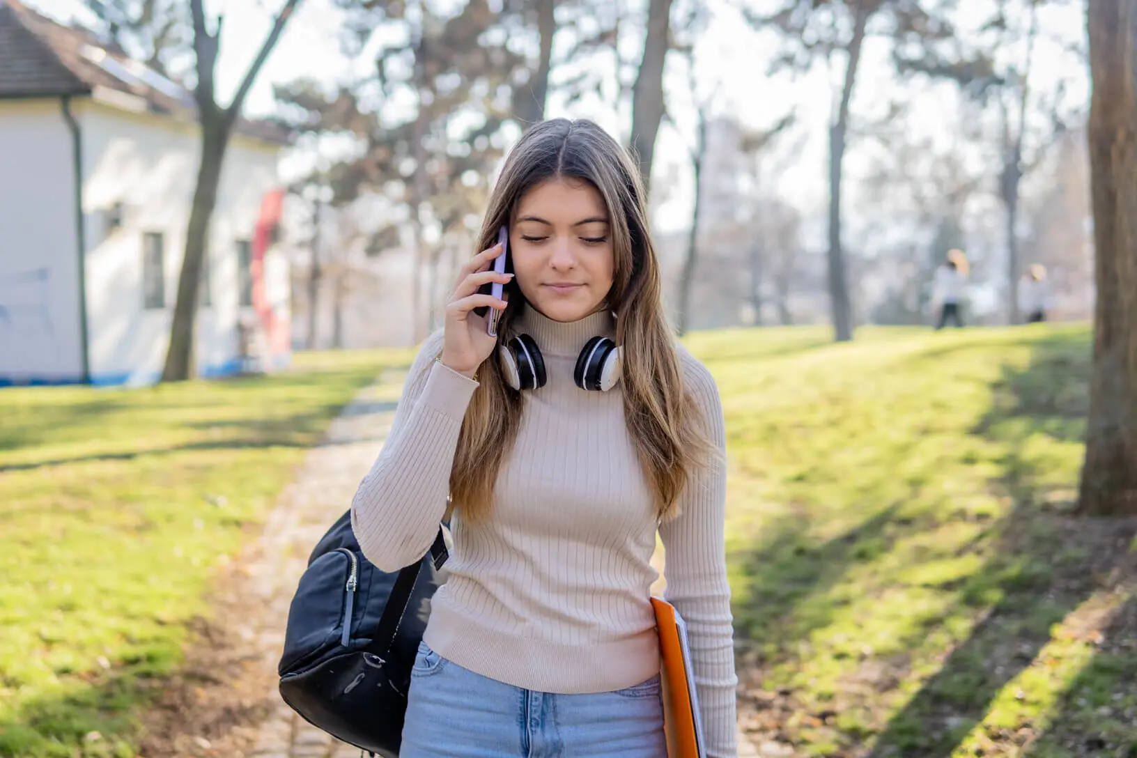 A young female student taking a phone call while walking through across campus.