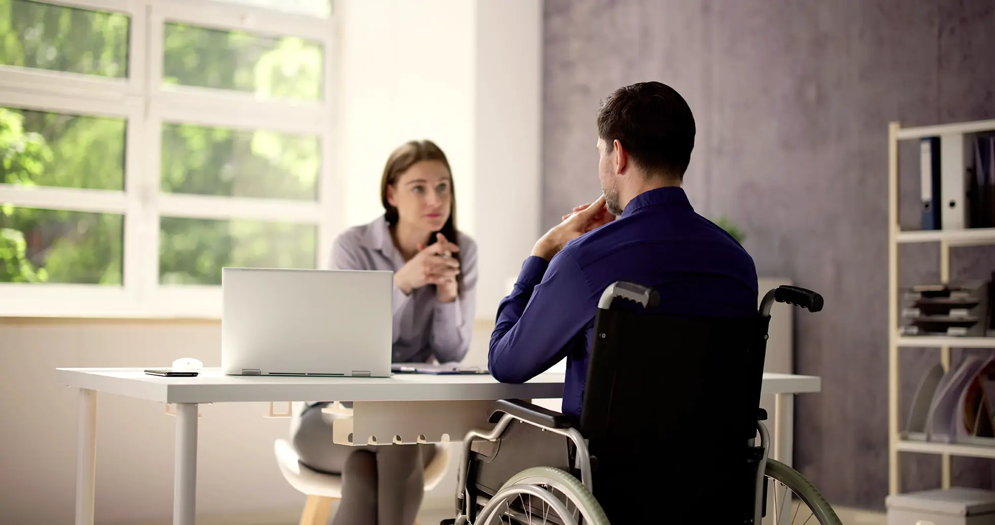 A man in a wheelchair talking to a woman in an office.