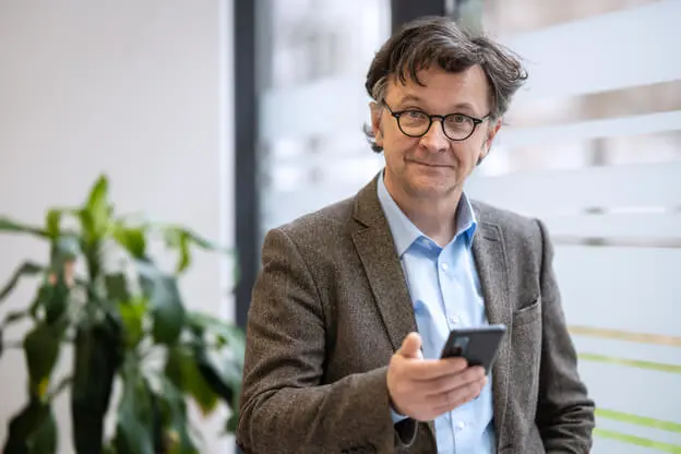 A mature man standing in his office using his phone.