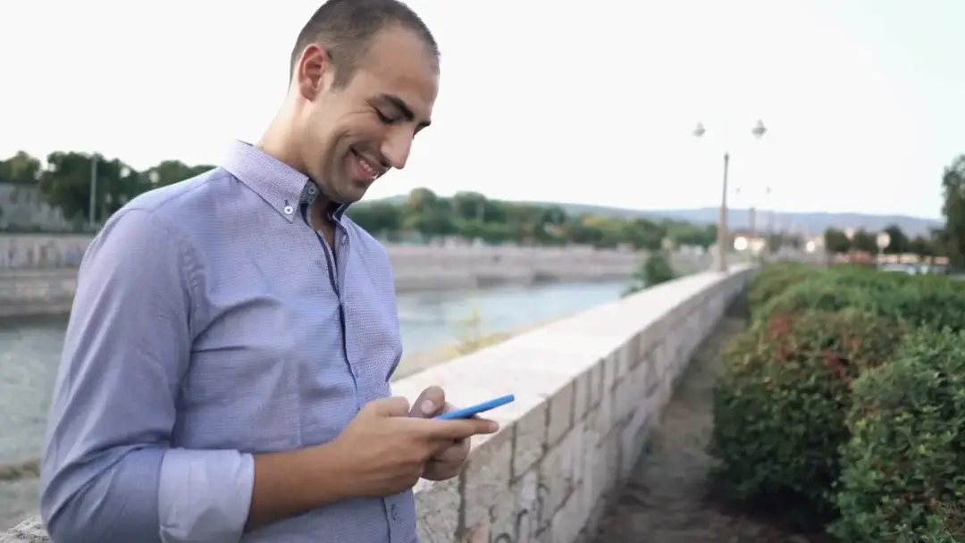 Geschäftsmann mit seinem Handy draußen an einem Fluss.