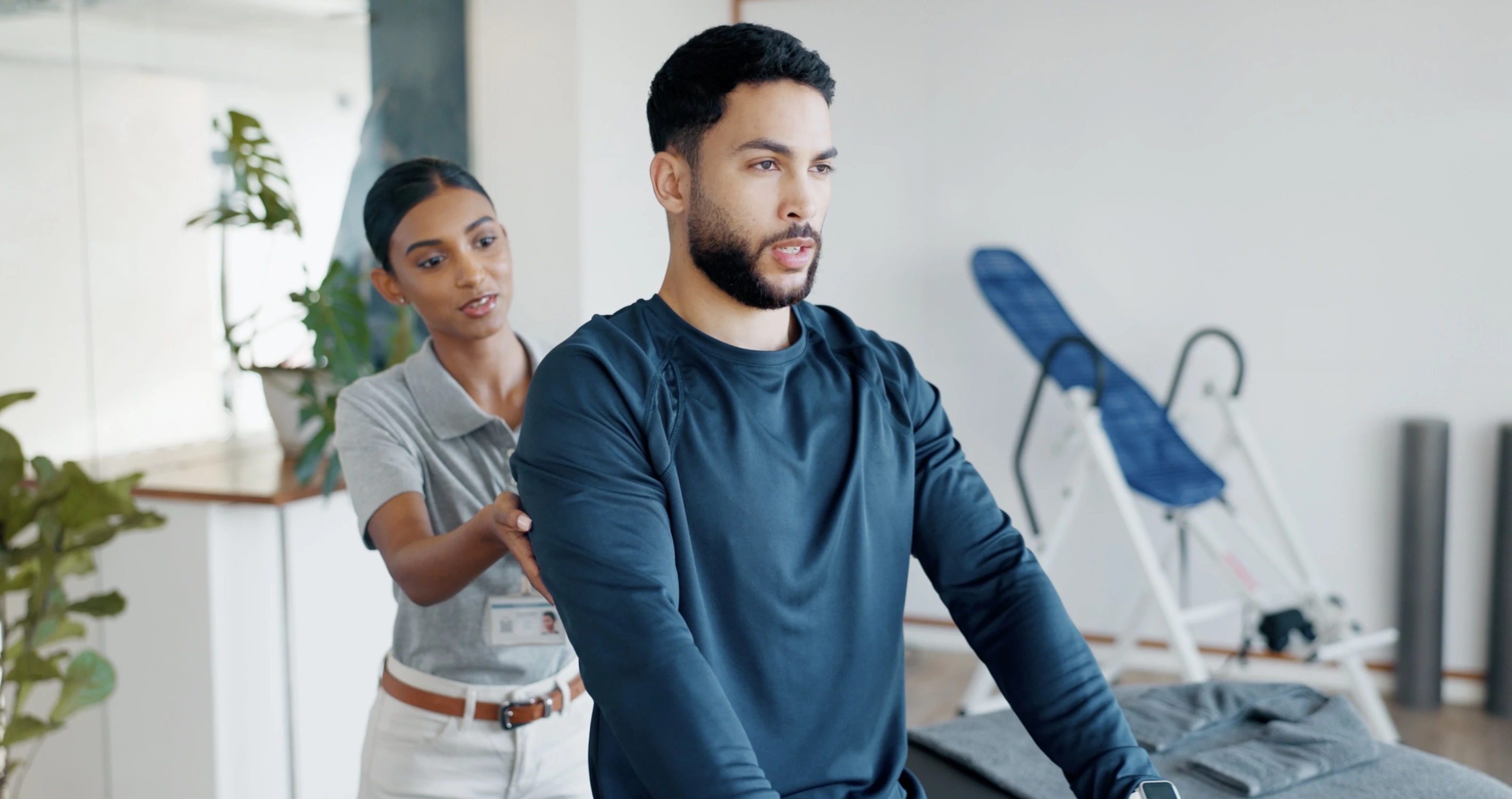 A man working out with dumbbells with a physiotherapist in a clinic.