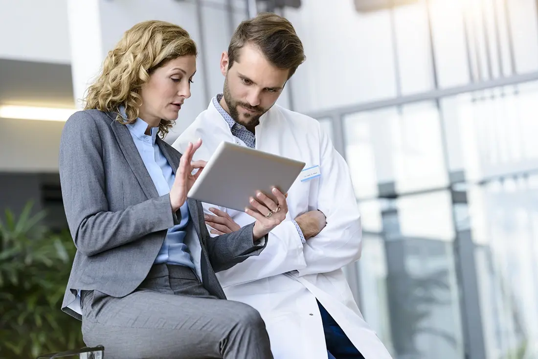 Een zakenvrouw met een tablet in haar hand in gesprek met een ziekenhuisarts