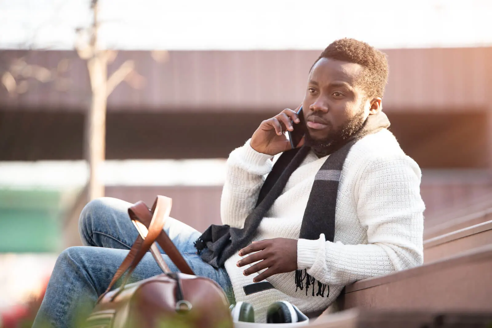 A young afro-american student sitting on a bench talking on his cellphone.