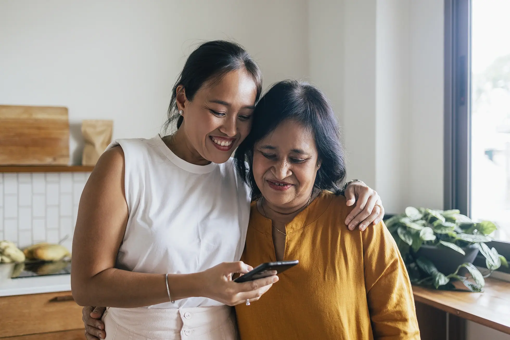 Asian mother and daughter looking at a smart phone in the kitchen.