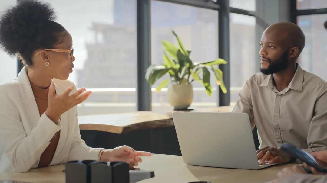 Een man achter een computer in gesprek met een vrouw op kantoor.