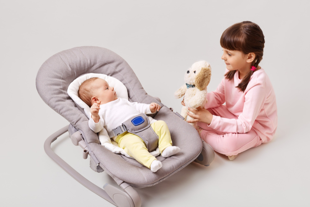 little-dark-haired-girl-with-pigtails-is-playing-with-her-newborn-sister-brother-who-is-lying-baby-rocking-chair