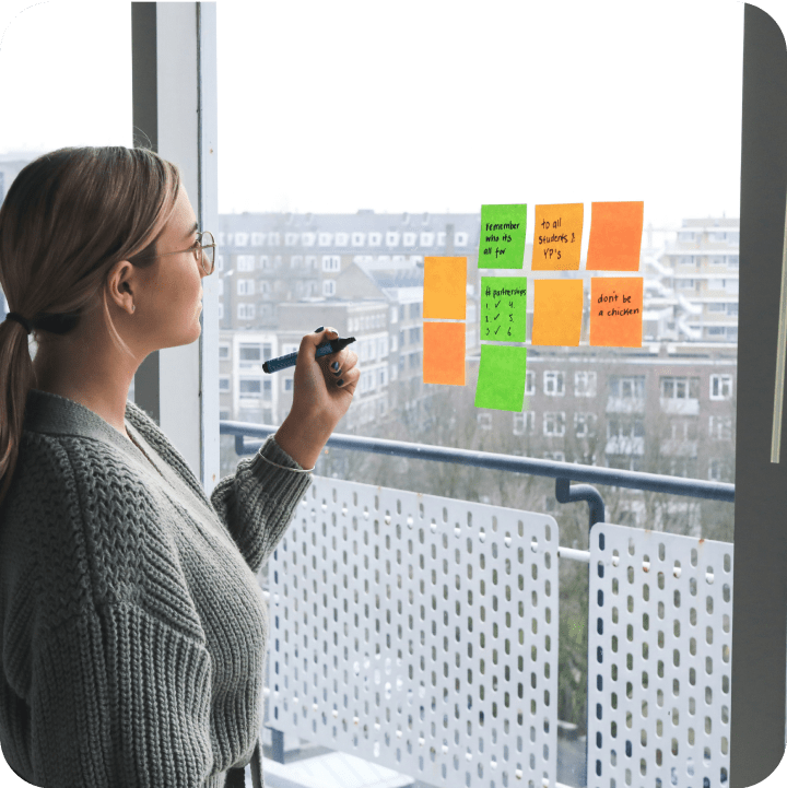 A person writes on colorful sticky notes arranged on a window, planning their future goals while overlooking a city view, representing the strategic path toward their veterinary career aspirations.