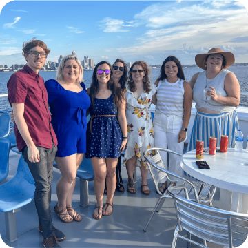 Embrace Pet Insurance employees enjoy a sunny day on a boat, showcasing diverse team members in casual attire smiling together, illustrating the company's emphasis on work-life balance and team bonding.