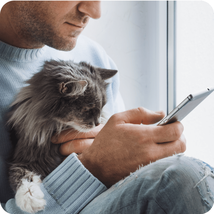 A man holding his cat while both curiously look at his phone, emphasizing the importance of understanding waiting periods in pet insurance policies before coverage begins. This moment reflects the need for pet owners to stay informed about their insurance options.