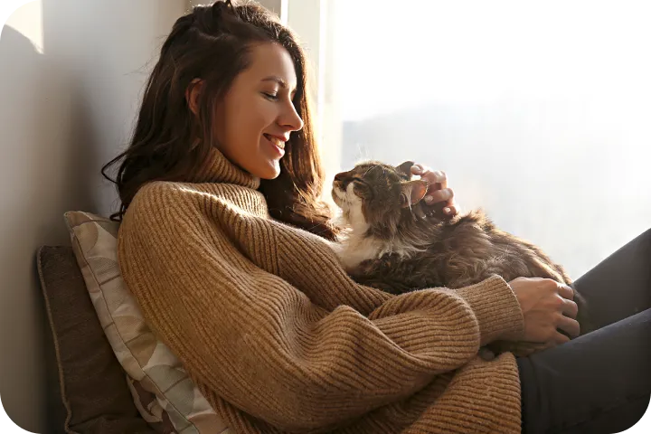 Image of a woman sitting on a chair with a long haired cat in her lap, gazing lovingly into each others eyes