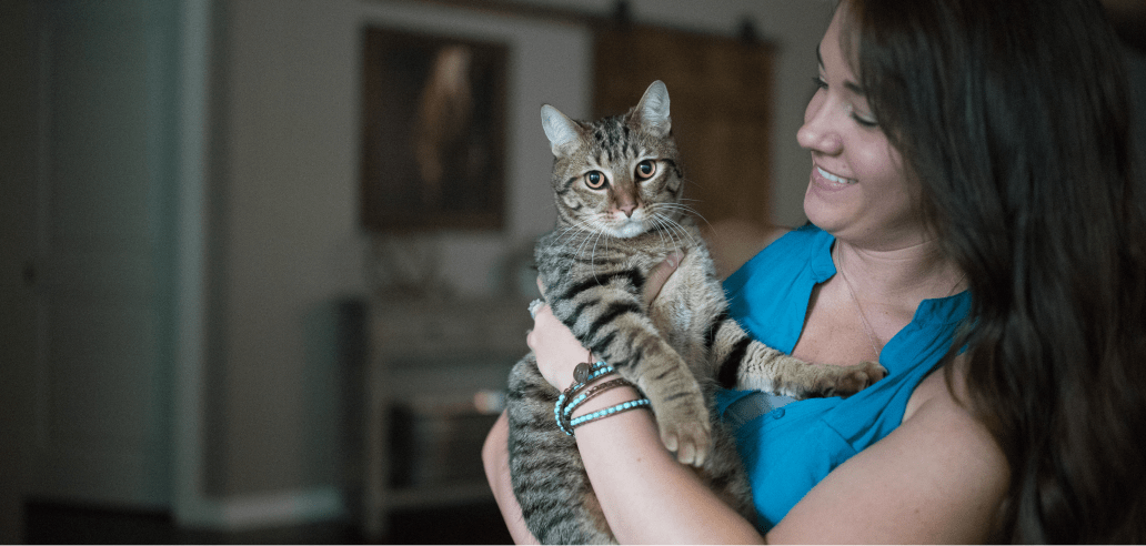 A woman in a bright blue top lovingly holds her adorable tabby adult cat