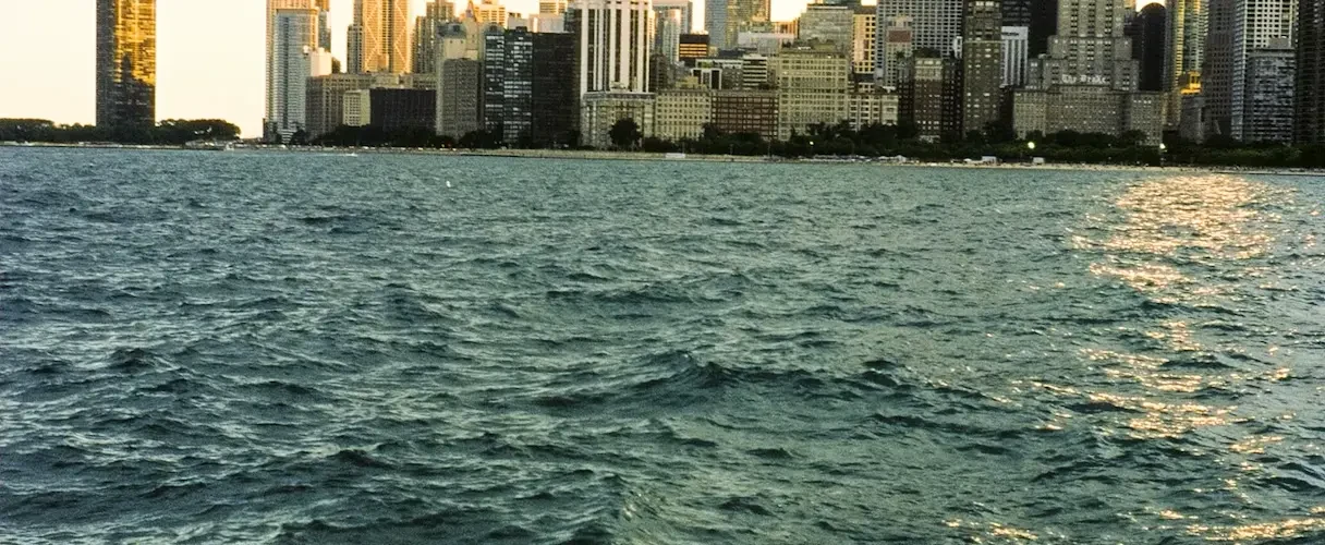A wide-angle view of the Chicago city skyline and skyscrapers seen from across the choppy blue water of Lake Michigan.
