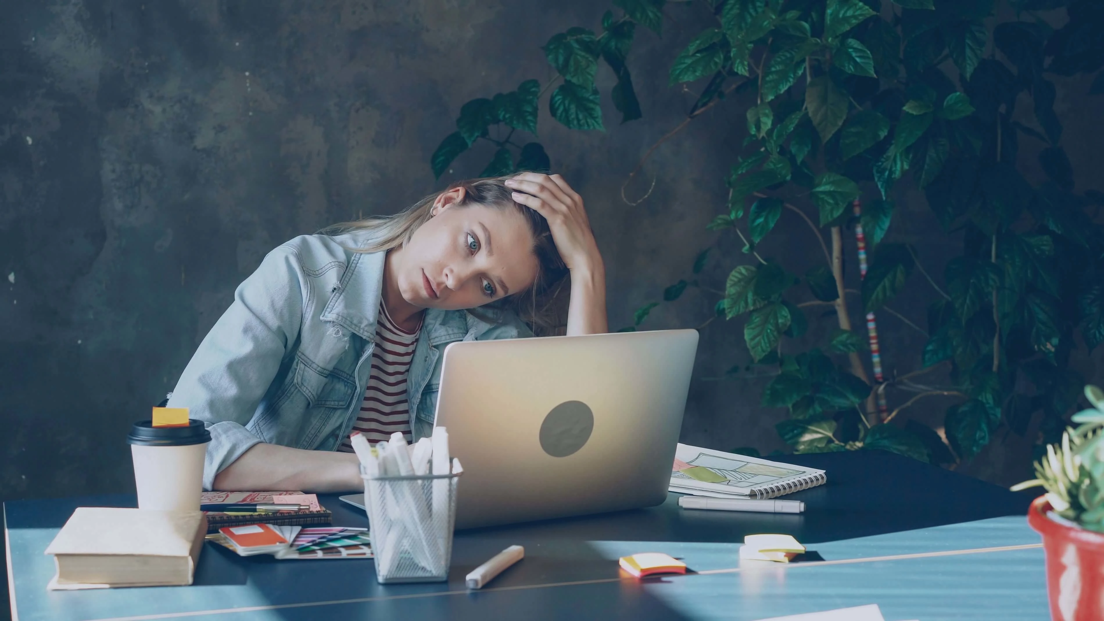 Woman in casual attire, deep in thought, working on laptop with coffee. Image by Vitaly Gariev.