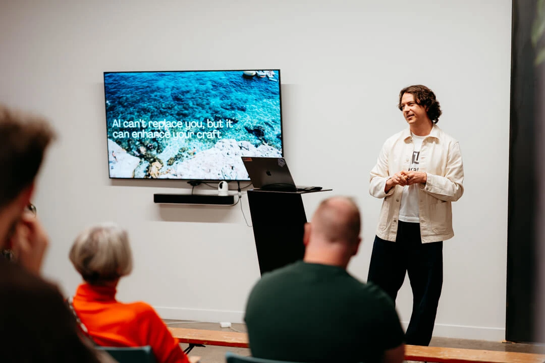 Narrative CEO & Founder James Broadbent giving a presentation to an audience in front of a screen displaying the text "AI can't replace you, but it can enhance your craft."