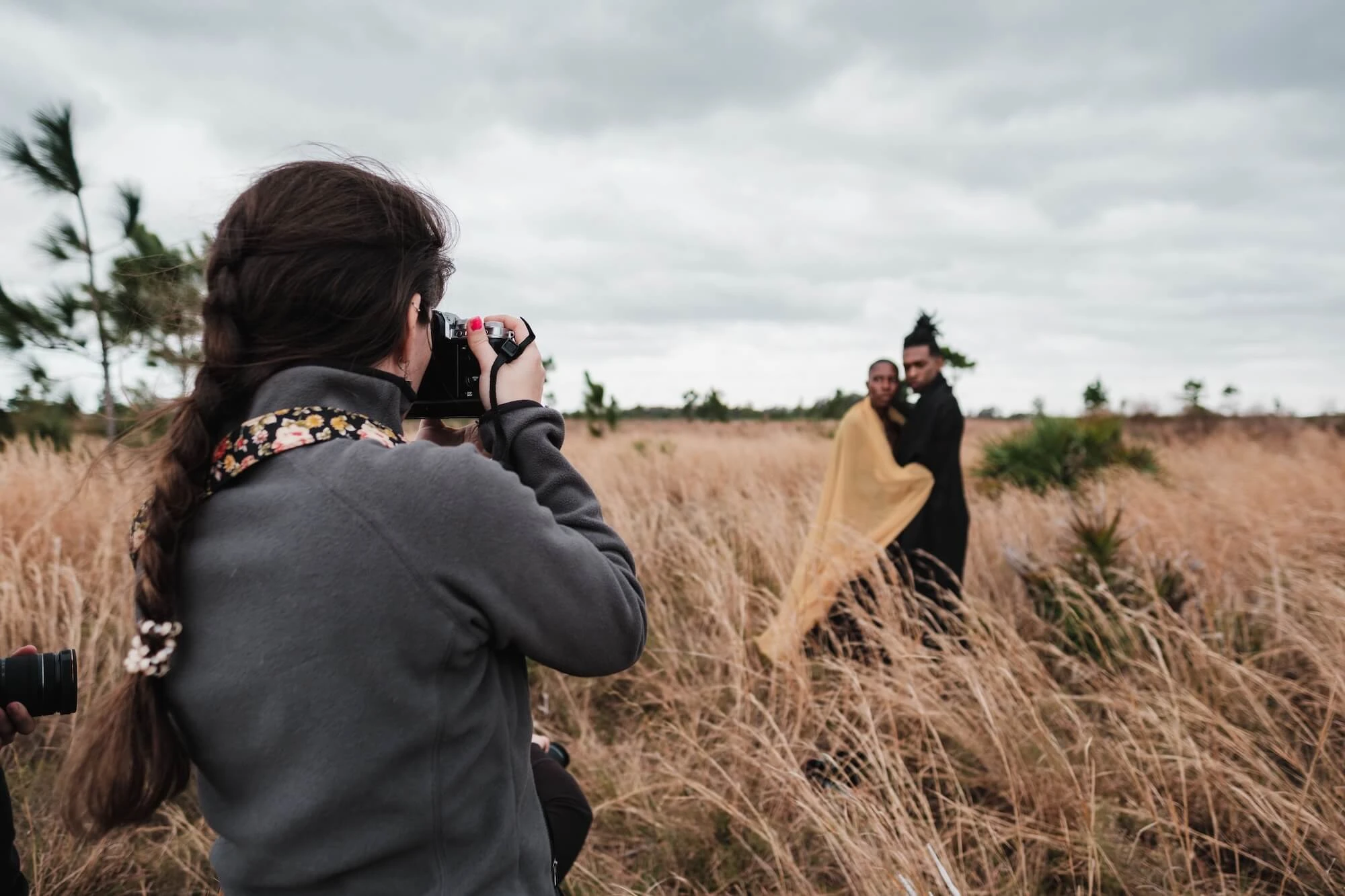A photographer takes pictures of a couple standing in a grassy field under an overcast sky. Image by Airam Dato-on.