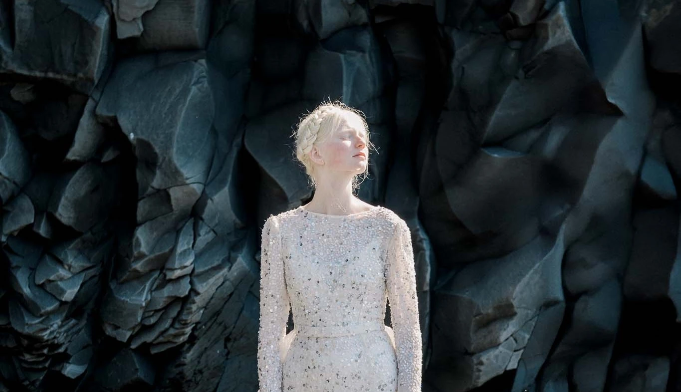 Elegant wedding dress displayed against a scenic Icelandic backdrop, featuring intricate lace and flowing fabric. Photo by Lisa Digiglio. 