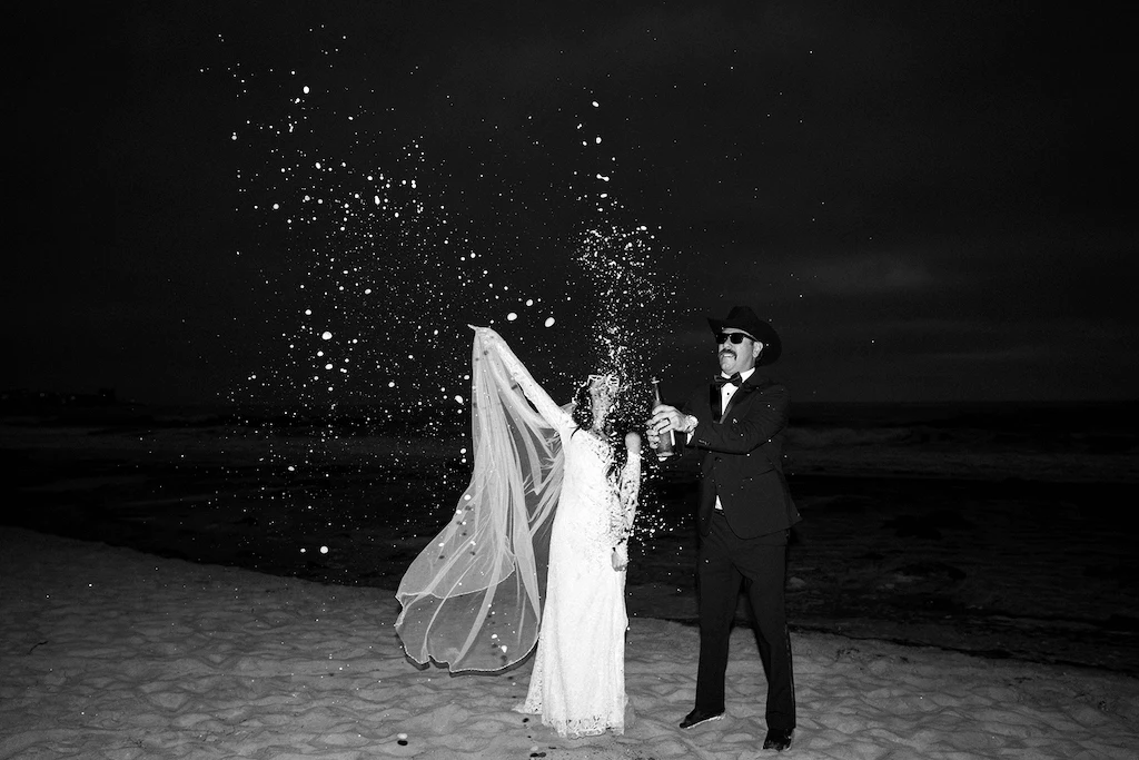 A bride and groom celebrate on the beach, surrounded by colorful confetti, capturing a joyful wedding moment.