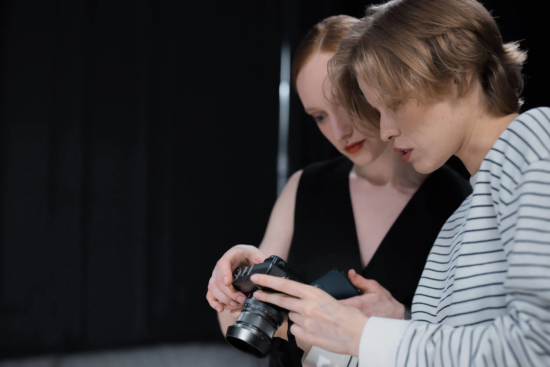 Two women examining a camera indoors with focused attention. Image credit to Ron Lach
