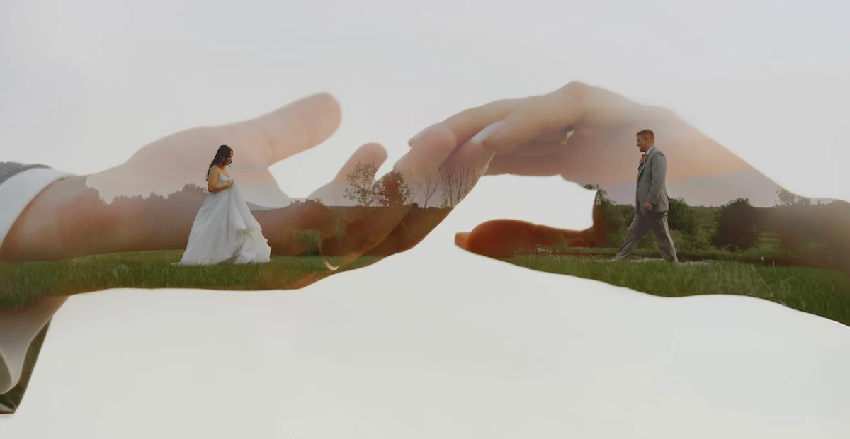 A double exposure photograph featuring two hands reaching toward each other, overlaying a bride and groom walking in a grassy field. Image by Dan Pinkard