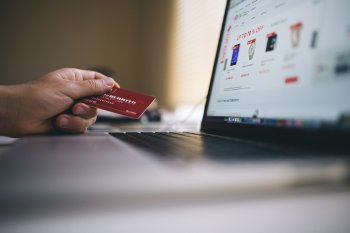 Hand holding credit card in front of laptop screen displaying an eCommerce website