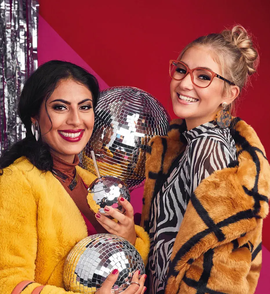 Two happy girls posing with big smiles holding sparkling disco balls.