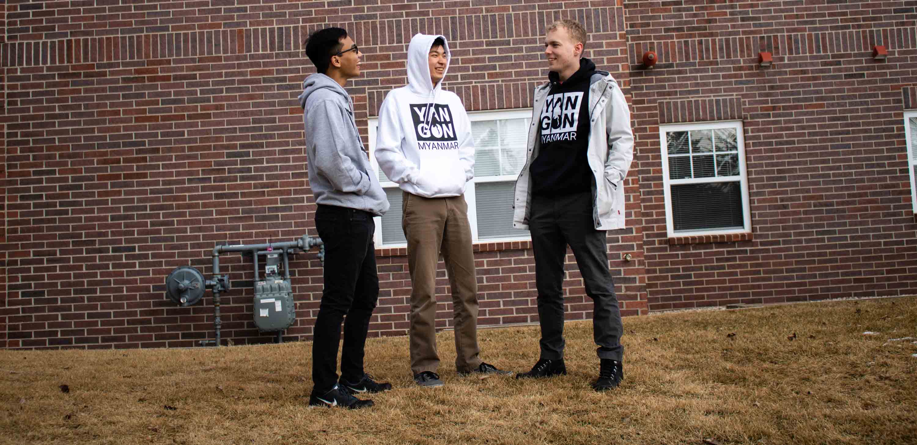 Three people talking in front of a brick wall