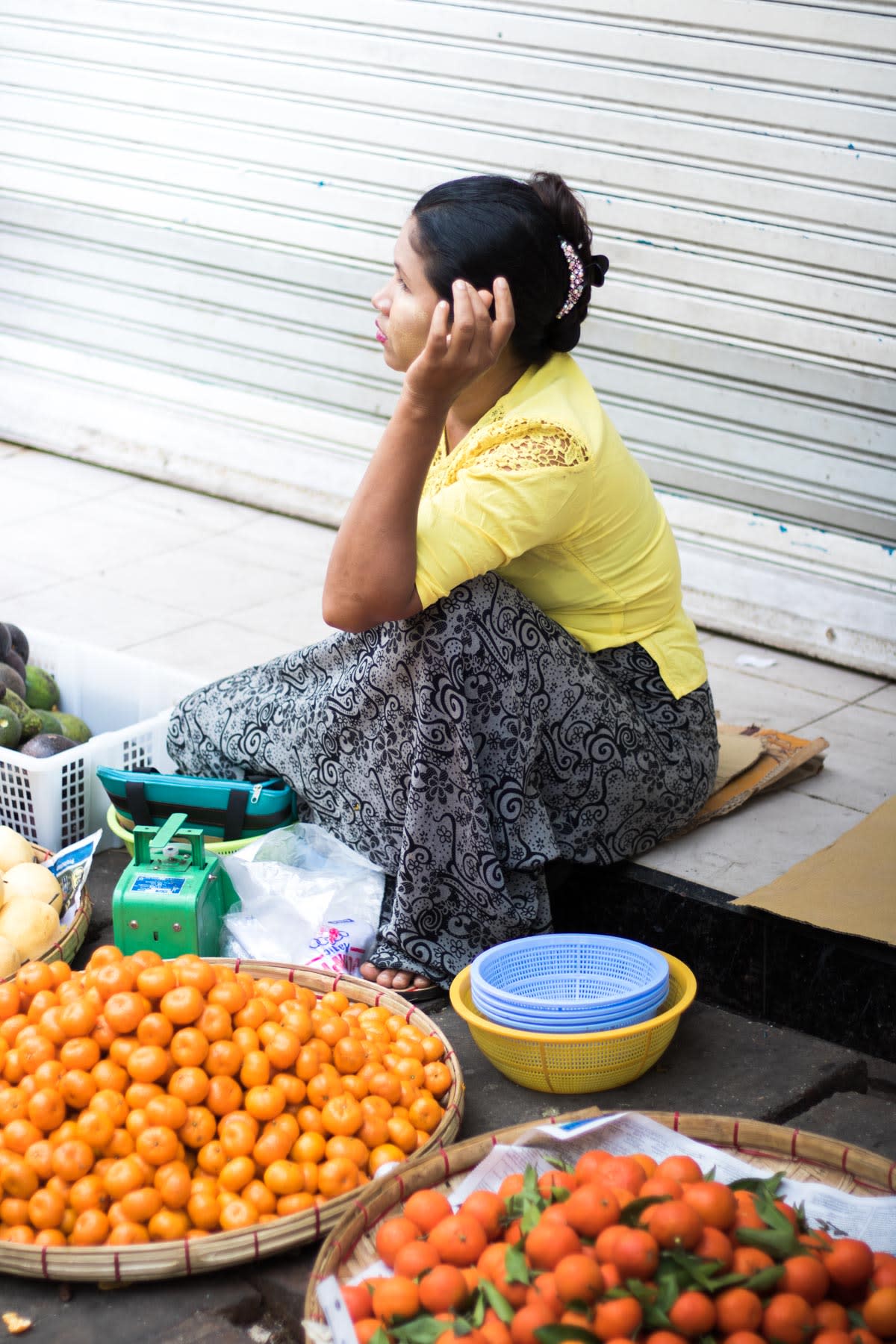 A fruits vendor sitting on curbside with tangerines on display