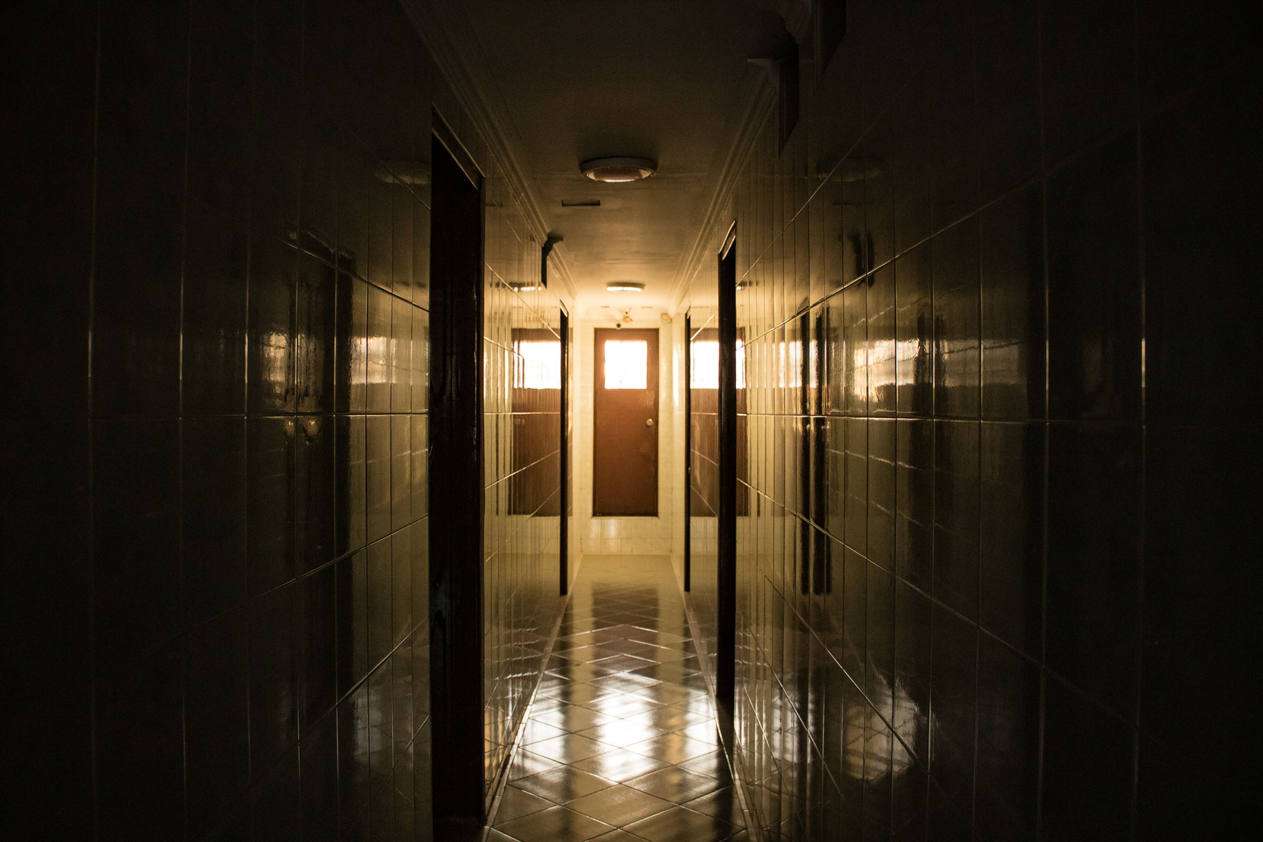 A ceramic-tiled hallway with a door at the end