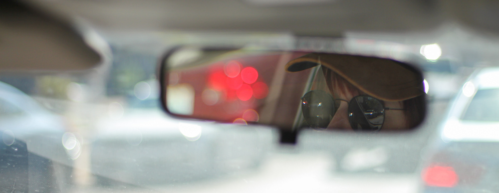 Person with yellow cap and dark sunglasses in view on rear-view mirror