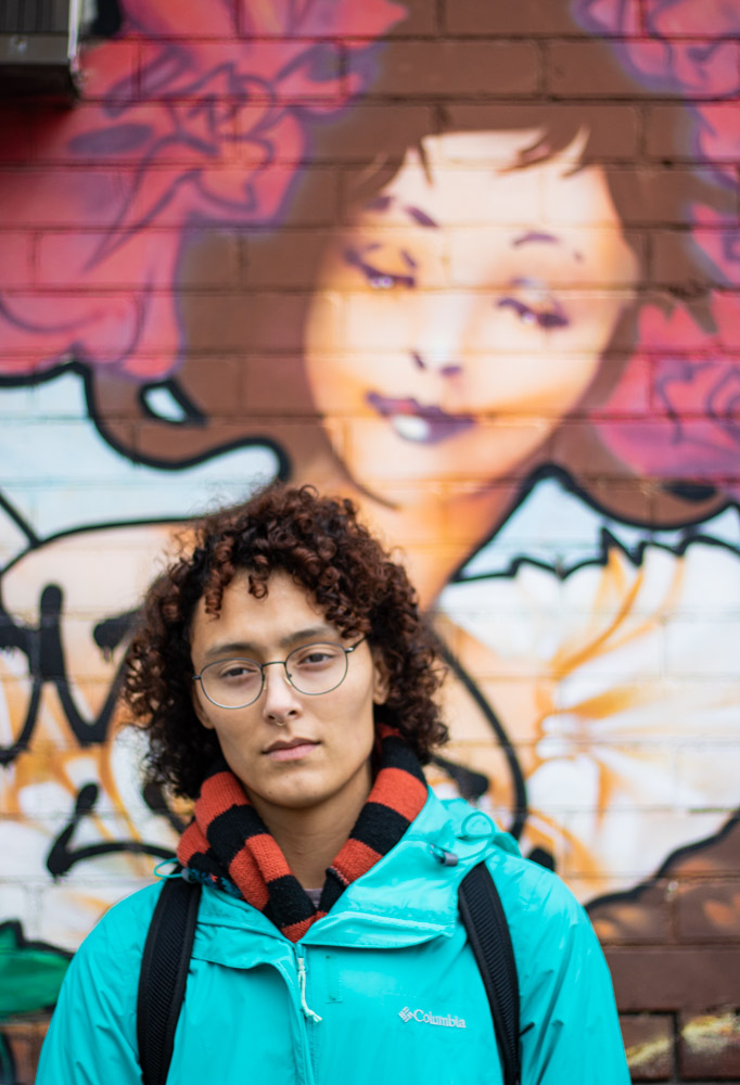 Person staring vaguely into the camera in front of graffiti