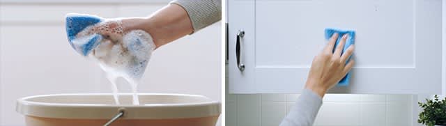 Hand squeezing soapy sponge above bucket and hand wiping cabinet with sponge