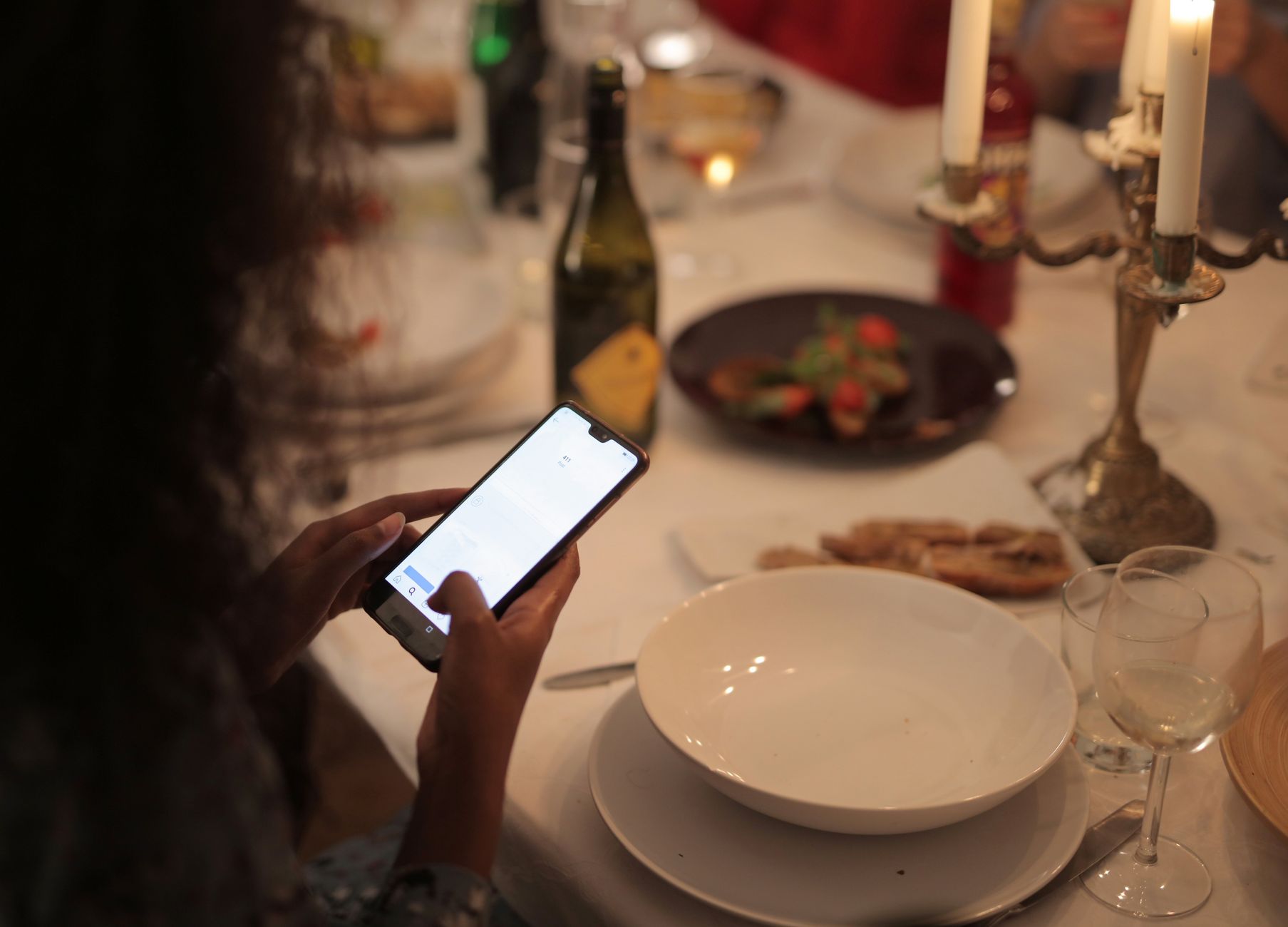 Eine Frau nutzt bei Kerzenlicht ein Smartphone an einem Restauranttisch · Foto: Andrea Piacquadio (Pexels)