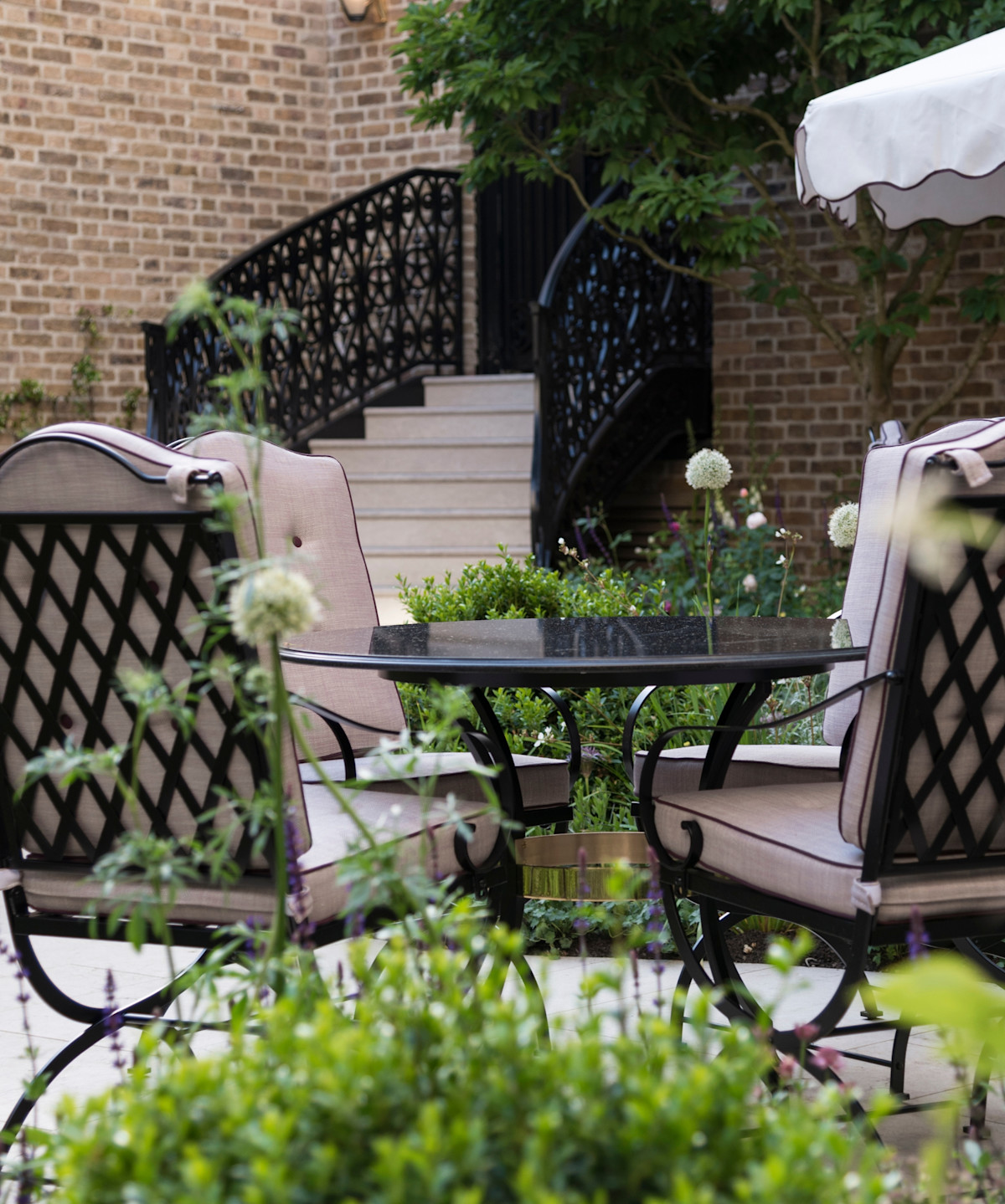 Cushioned patio chairs and table surrounded by lush garden plants