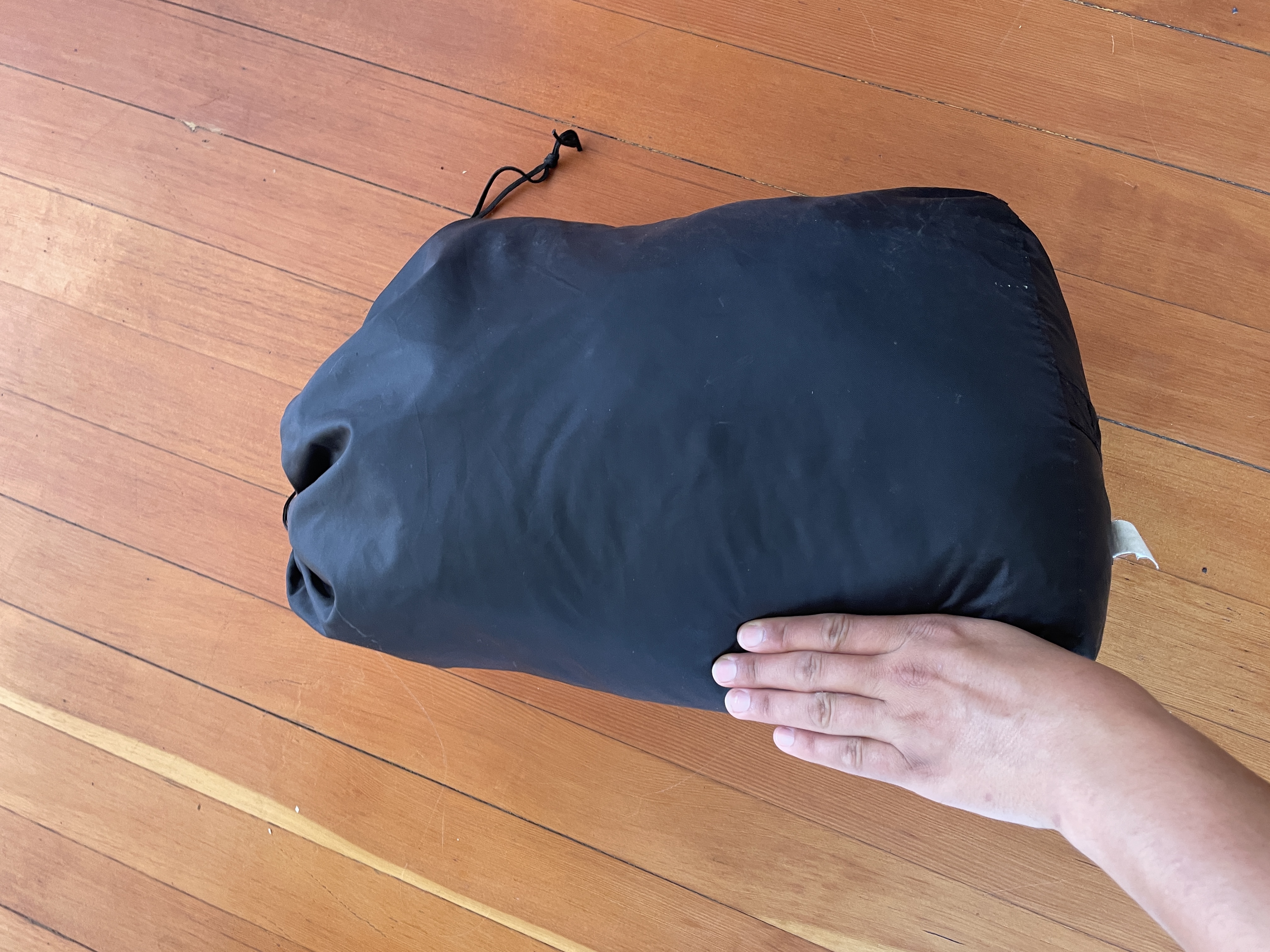 A picture of a sleeping bag packed in a stuffsack with a hand next to it for scale. The hand is approximately 1/3 of the height of the stuffsack and 1/4 of the width.