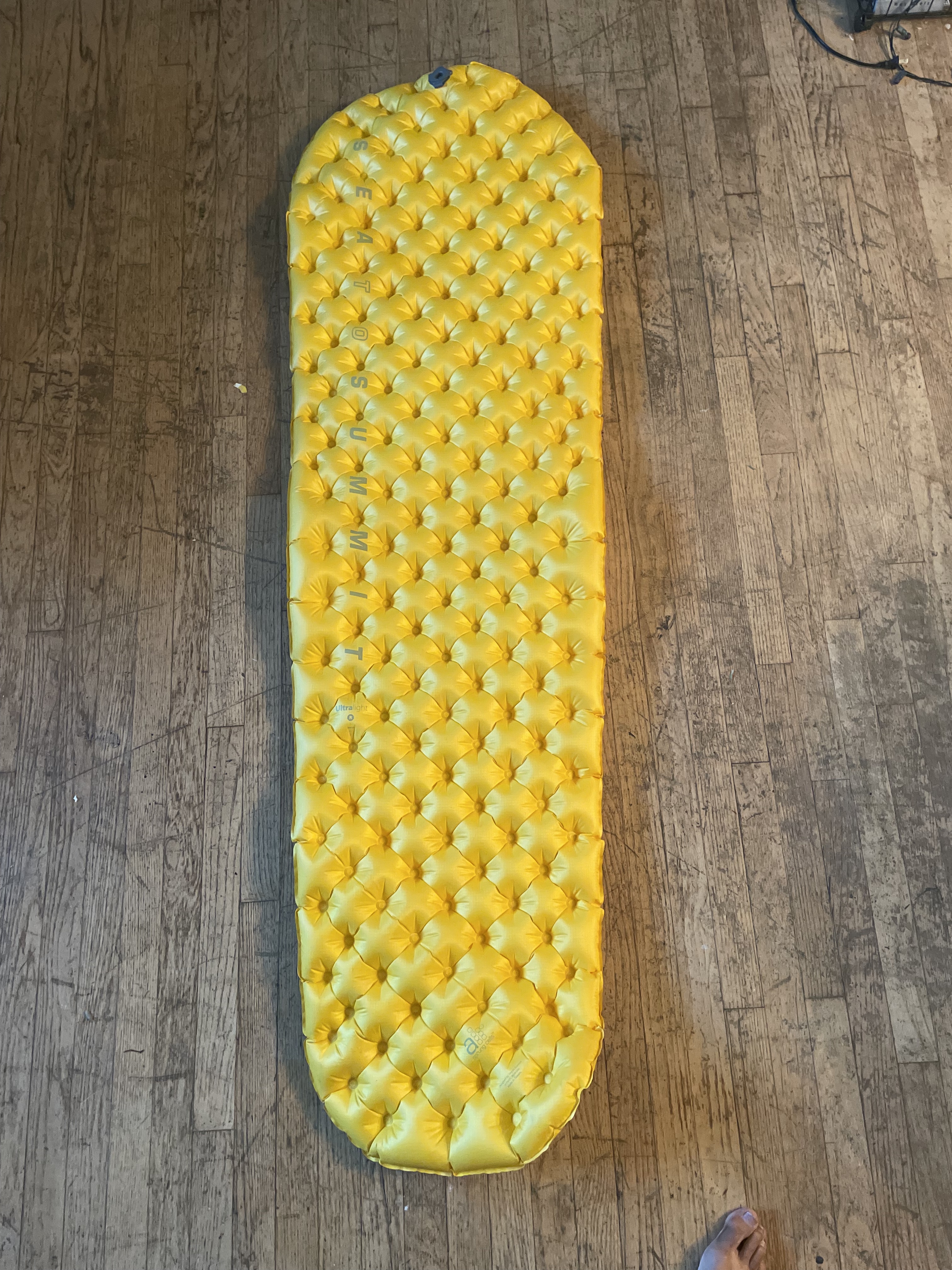 A picture of a thin yellow sleeping pad with a hexagon pattern of inflated portions, with a slight taper from the head to the foot of the pad.