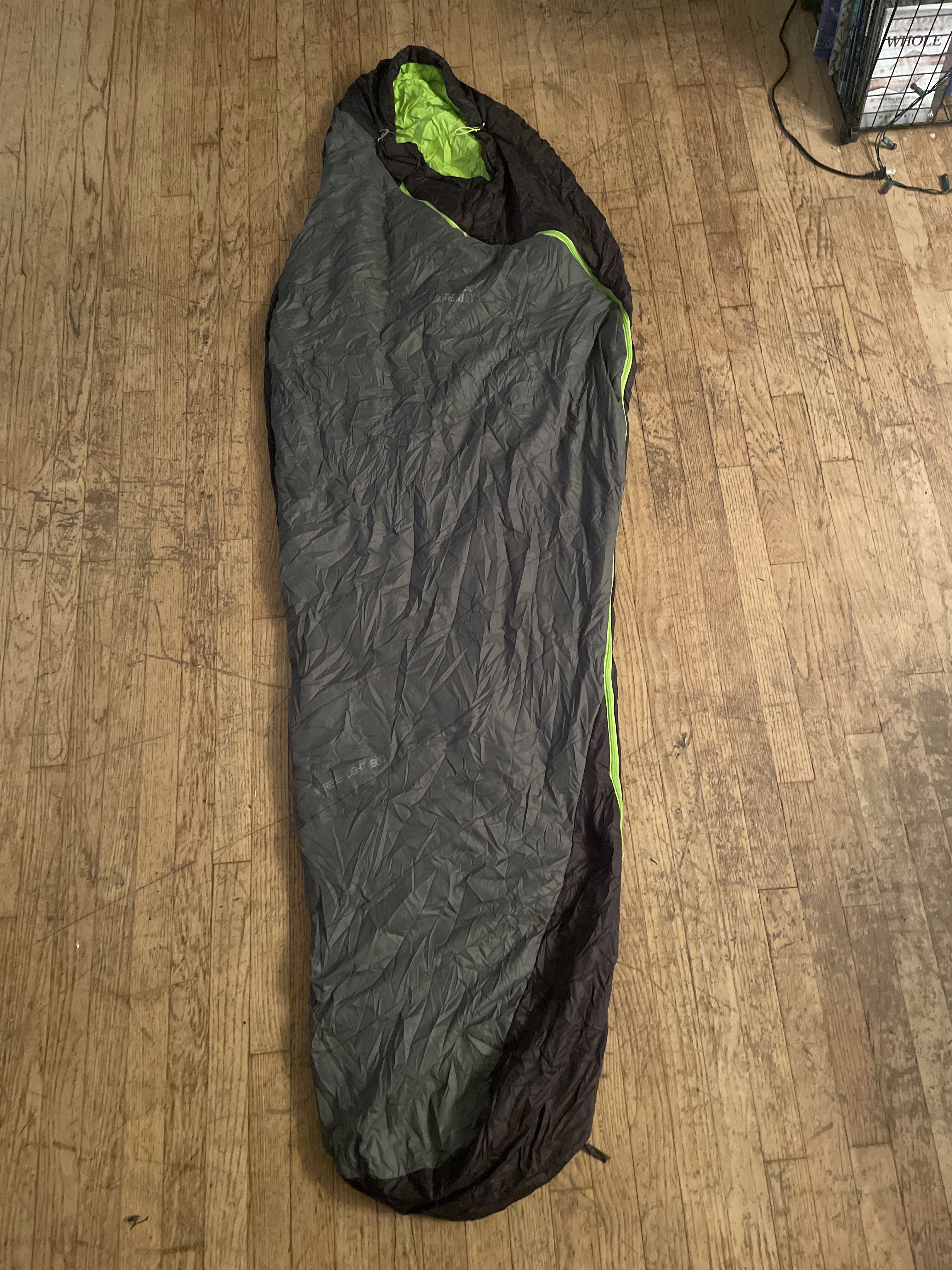 A picture of a wrinkled grey mummy style sleeping bag with a light grey outer layer and neon green inside lining.