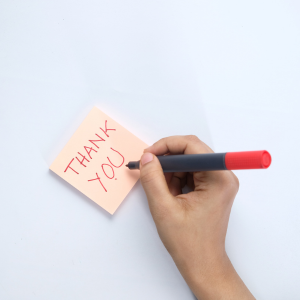 Women’s hand writing THANK YOU top down on a paper note, using a red marker.