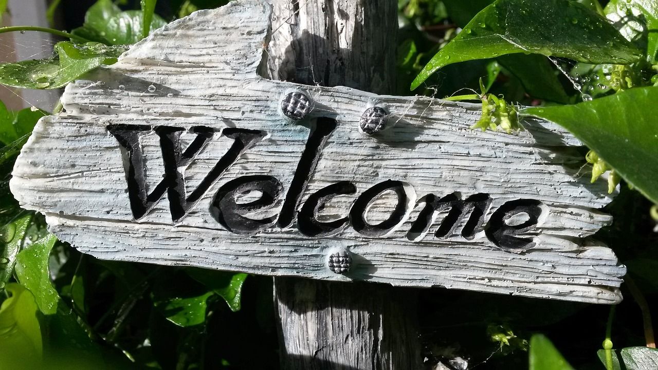 Wooden welcome sign with a background of green leaves.